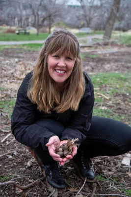 Woman kneels down holding a hand full of acorns.