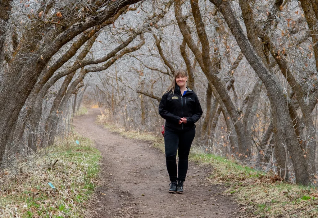 Woman stands on a path surround by dead trees.