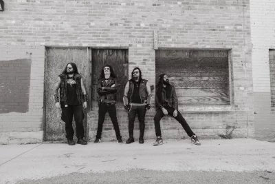 Four guys leaning up against a brick wall.