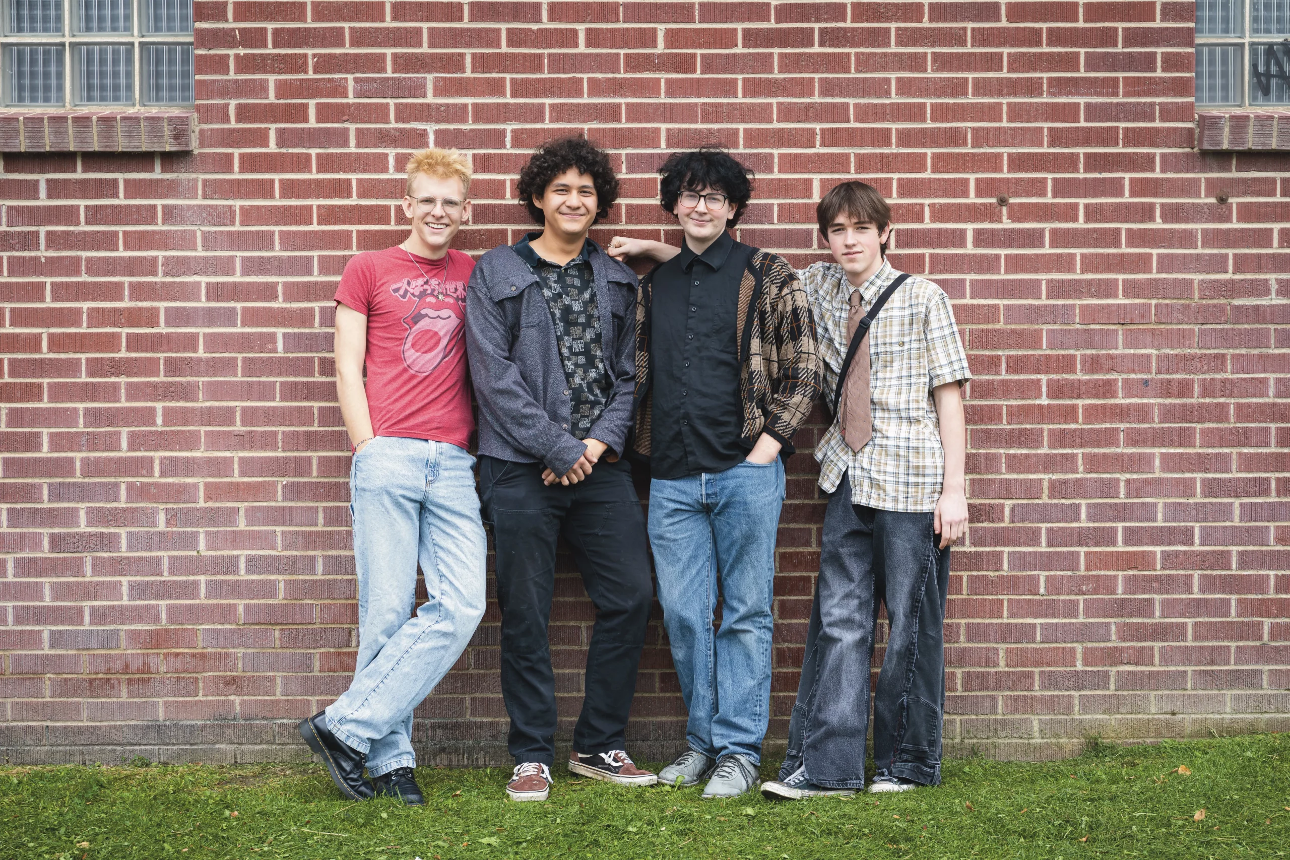 Four guys standing in front of a brick wall.