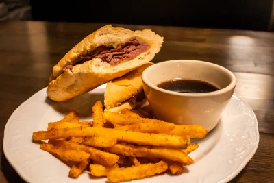 The French Dip sandwich at Two-Bit Bistro served on a plate with au jus and fries.