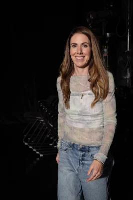 Playwright Morag Shepherd stands and smiles in front of a black backdrop.