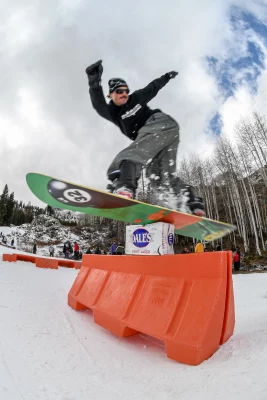 Snowboarder Pat Fava does a backside lipslide over a pack of beer resting on an orange barrier at Brighton Resort in Brighton, UT.