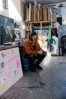 Andrew Alba squats near kids art in his studio