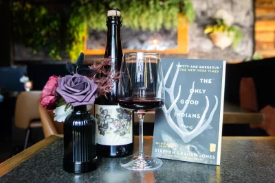 The next Books Take Flight book choice posed next to some wine