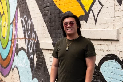A man standing against a mural in a downtown area.