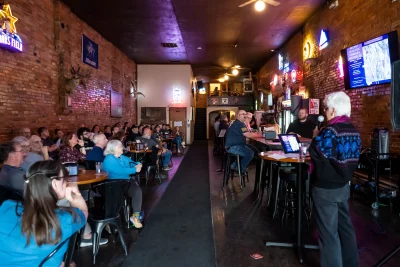 People gathering around a woman speaking at a bar.