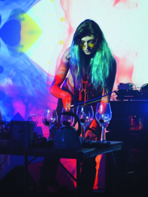 Hal Jean stands before a table of wine glasses in multicolored light and smoke.