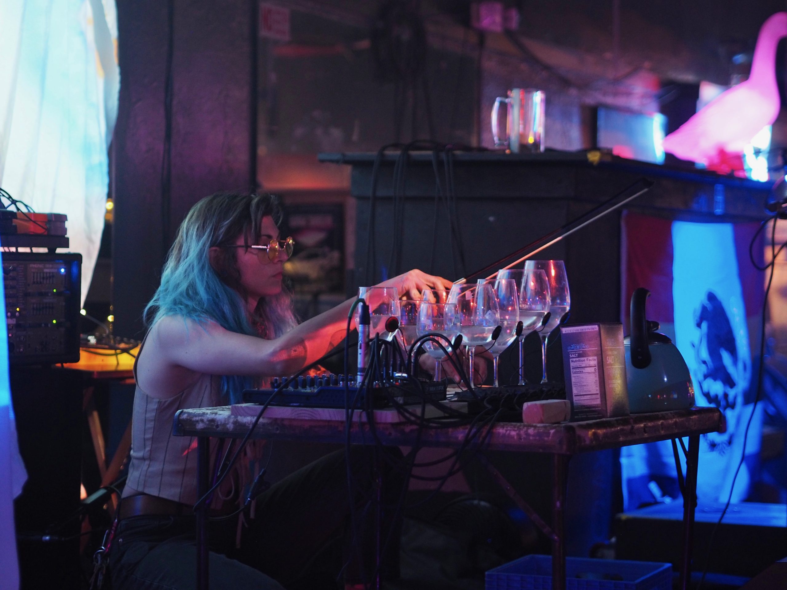Hal Jean crouches in front of a row of wine glasses filled with water, playing music.