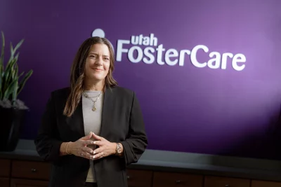 Utah Foster Care CEO Nikki MacKay poses in front of a purple wall with the logo