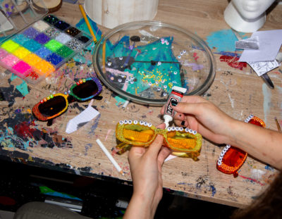 Creator of Silly Little Guys shares insight into her artistic process and creative workspace while gluing beads and gems onto a pair of sunglasses.