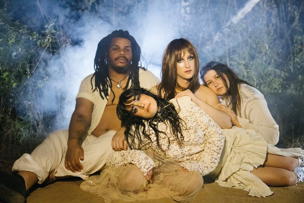The members of Mannequin Pussy sit together, all wearing white and surrounded by fog.