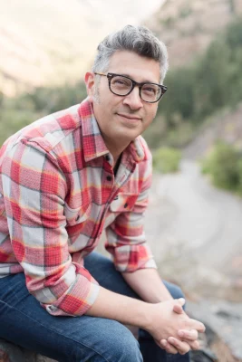 The profile photo of University of Utah professor and novelist Michael Mejia, where he's seen sitting down on a rocky trail and leaning toward the camera.