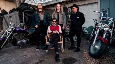 Four bandmates sitting in a circle next to motorcycles.