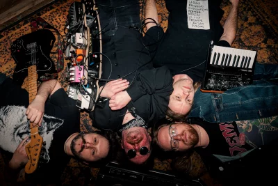 The four bandmates laying on the carpetted ground.