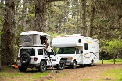 An RV and a Jeepwith a camper tent on top, parked next to each other.