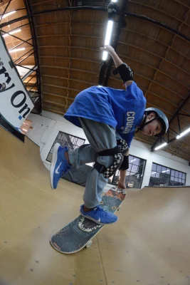 A young skater in a blue shirt pulls off a skating trick inside an indoor skate bowl.