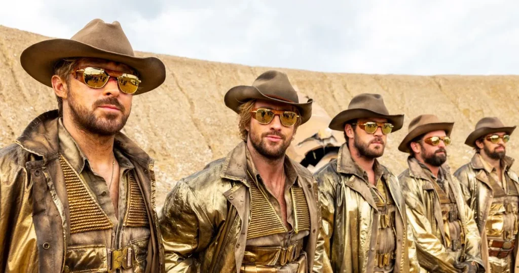 Five men in the exact same outfit, consisting of big sunglasses, a cowboy hat, and leather jacket, all stand in a row in the desert.