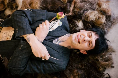 Gravess lyinig in a pile of hair holding a rose and sticking out their tongue. 