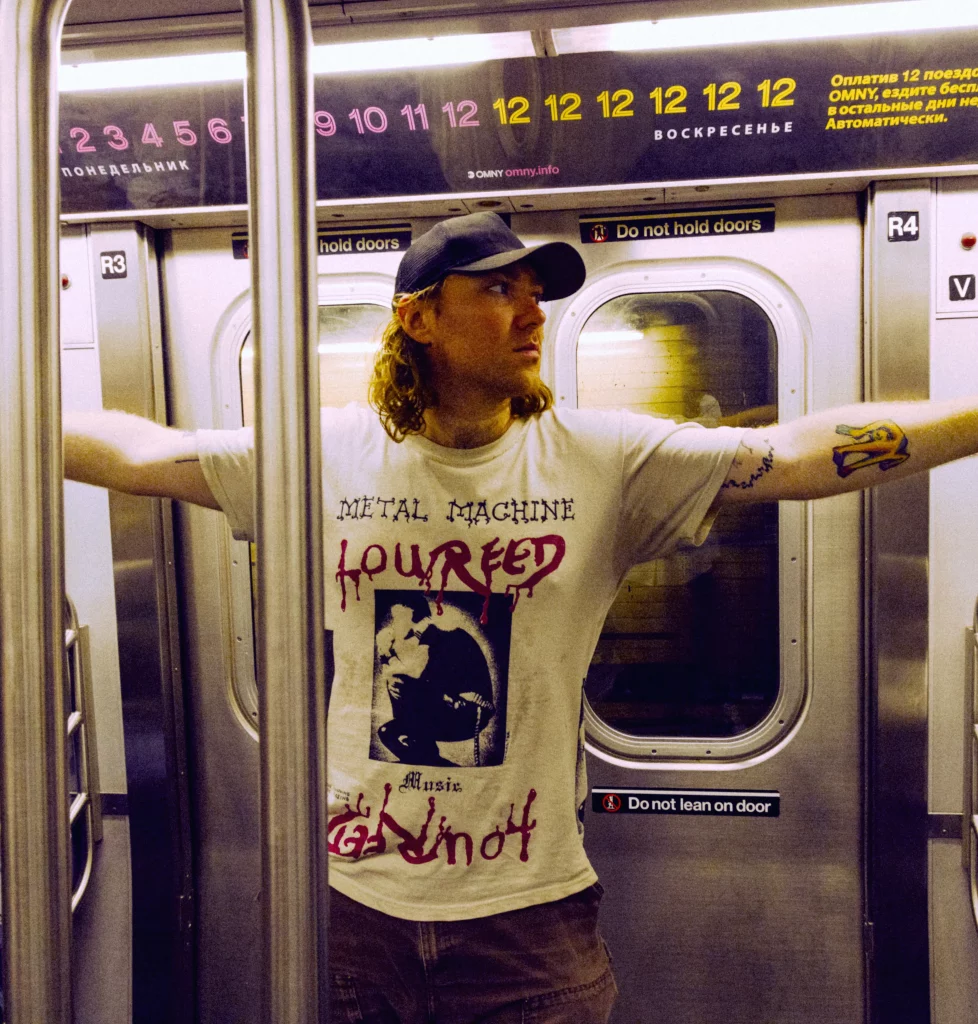 Nick Rattigan stands in a subway with arms outstretched.