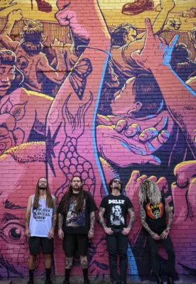 Masculine humans stand with a cool vibe against a colorful brick wall, covered in graffiti art.
