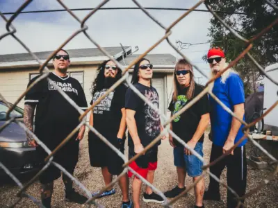 Men stand behind a grated fence, staring at the camera slightly tilted in body angle.