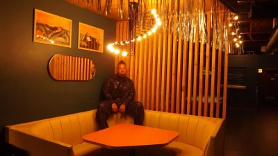 Icky Rogers sitting on back of booth in room with orange lighting.