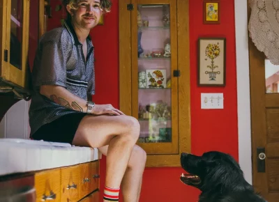Peter Goldie sits on a countertop with a black dog looking up at him.
