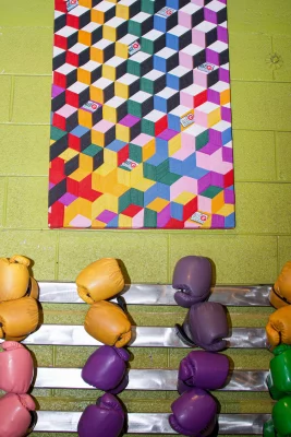 Colorful abstract art hangs on a bright green wall above a rack of multi-colored boxing gloves. 