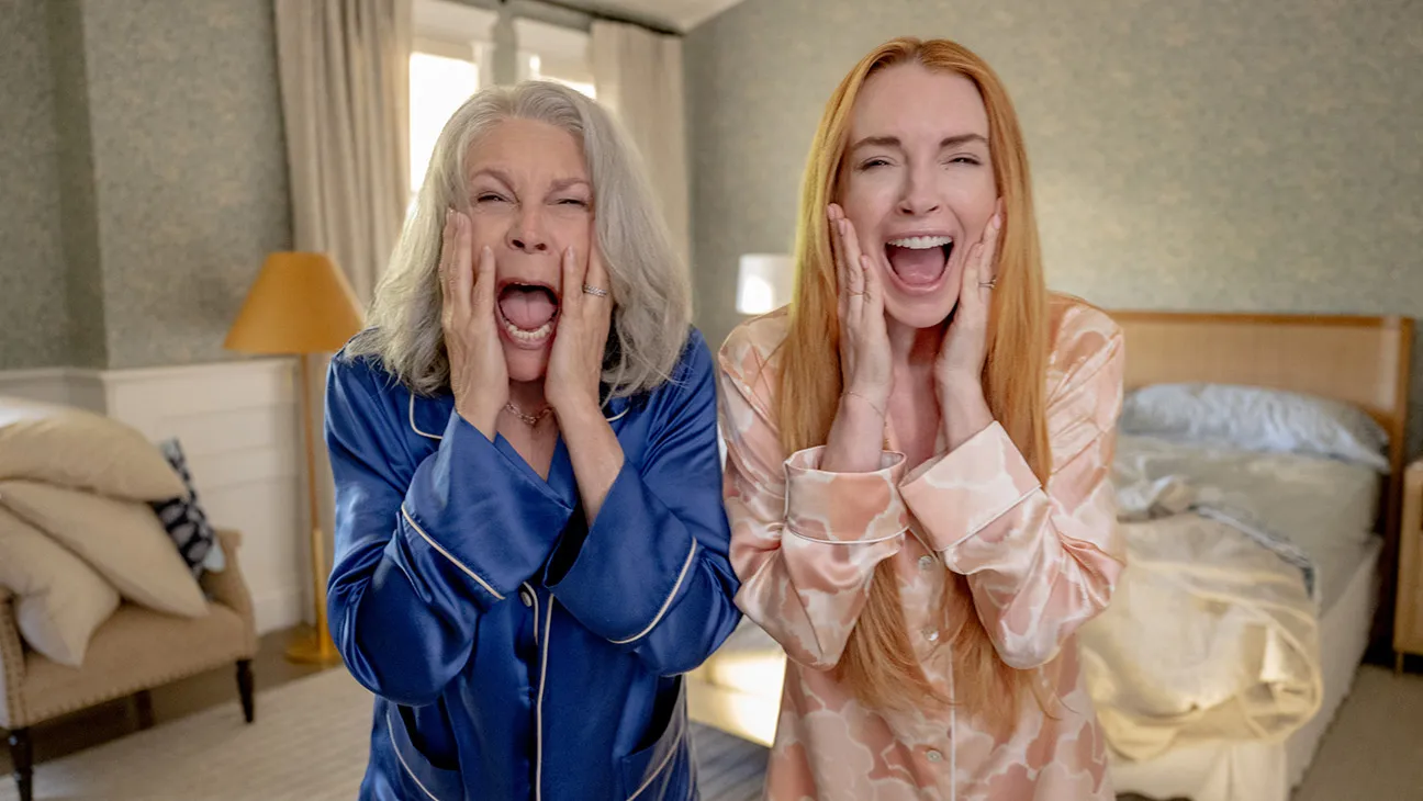 Lindsay Lohan and Jamie Lee Curtis stand with their hands on their face and a shocked expression.