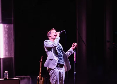 Damian Kulash, lead singer for OK Go, singing at the mic with bandmates just out of frame, on stage in Salt Lake City UT.