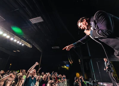 Pelle Almqvist leaning over, pointing at the audience while playing on stage in Salt Lake City for the new album release of The Hives Forever Forever The Hives.