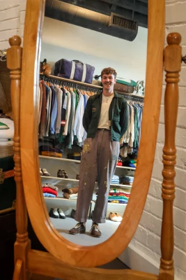 Vintage clothing retailer Dillon Firestein standing in front of a mirror in his store, Quotidian Ragazine, in Salt Lake City.