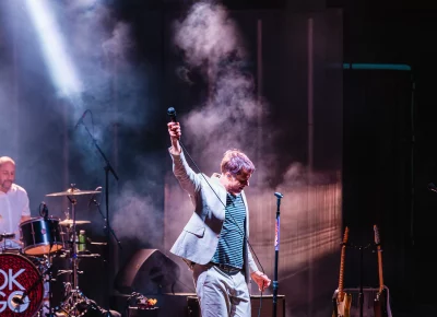 Damian Kulash of OK Go raising his arm and mic to the air with the crowd singing back the lyrics as the music plays.