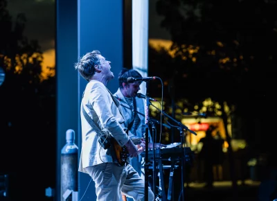 Lead singer Damian Kulash (front) and Andy Ross on keyboard (back) on stage and bathed in the blue backlighting as the sun has fully set in the background. Shot on stage in Salt Lake City, UT at the Red Butte Garden Amphitheatre.