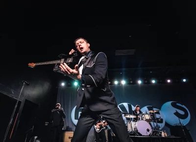 Niklas Almqvist of The Hives, raises his guitar in one hand, and gestures to the audience with the other to encourage more noise!
