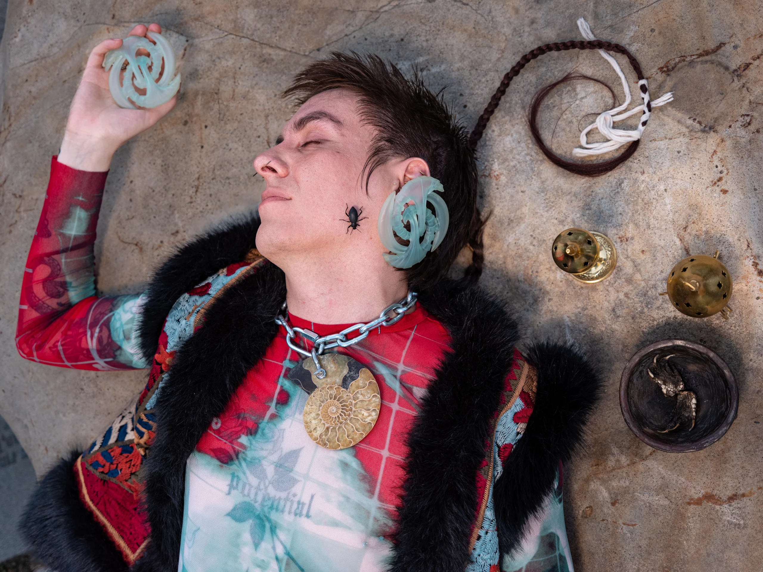 Arthur Diaz lying on a rock with a beetle on their face surrounded by accessories.