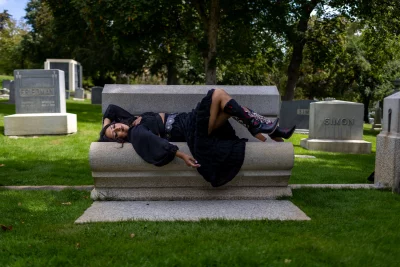 Litzi Estrada laying on a bench in a graveyard.