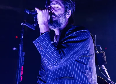 Lead vocalist Ben Schneider of Lord Huron at the mic, singing as he is surrounded in blue lights coming from the stage.