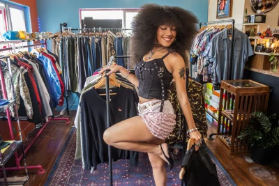 Adaline Rae standing in front of clothes racks wearing a black corset-like top with straps and pink lacy shorts.