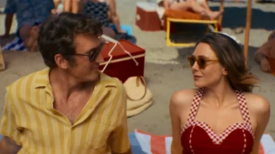 Miles Teller and Elizabeth Olsen look at each other while sitting on the beach in Eternity