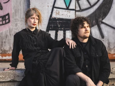 Joe and Shelby Maddock of the Plastic Cherries pose in all black against some graffiti