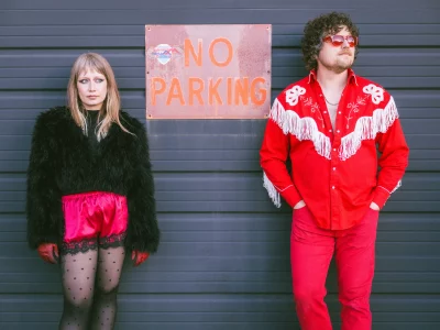 Joe and Shelby Maddock of the Plastic Cherries pose next to a "no parking" sign in red outfits