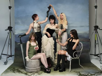 The five members of The Last Dinner Party pose in Victorian garb in front of a blue backdrop for an official photoshoot.