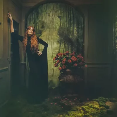 Florence Welch from Florence + the Machine poses against a wall with greenery lining the floor and doorway