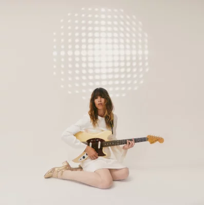 Melody Prochet of Melody's Echo Chamber kneeling with her cream colored electric guitar.