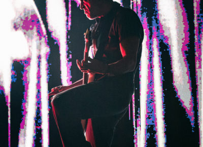 Julio Tavarez touring bassist for Bob Moses, pictured in front of a giant LED wall, playing during the set and looking at fellow band members while on stage in Salt Lake City.