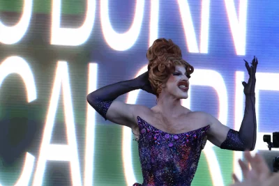 A drag queen in front of a giant screen.