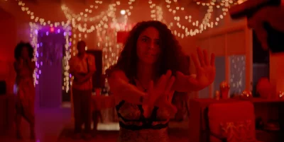 A woman in a red room with a gun pointed at her.