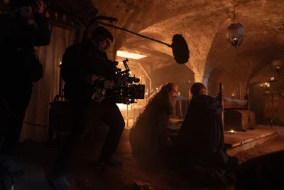 A scene from the set of The Death of Robin Hood. Two characters sit in a dim tavern with a boom mic in the background.